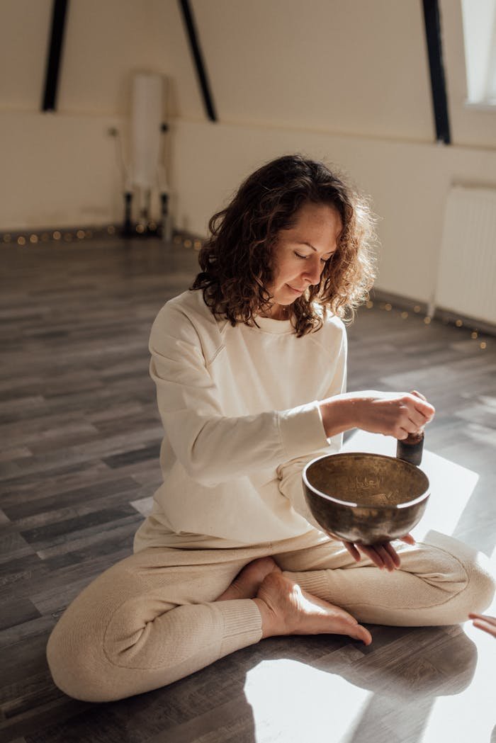 services-04 A woman in a peaceful meditation pose indoors, using a Tibetan singing bowl to enhance relaxation.